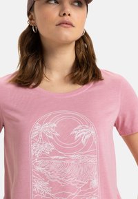 Camiseta de algodón rosa con un gráfico contorneado en blanco de un paisaje costero con palmeras y olas en un diseño arqueado. Mangas cortas.