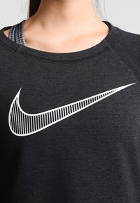 Felpa nera con collo rotondo, caratterizzata da un grande logo Nike bianco con dettagli a righe sul petto. Tessuto testurizzato, vestibilità atletica.