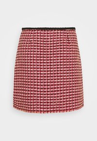 Mini-jupe en tweed rouge et rose avec un motif à carreaux texturé, bordée d'une ceinture noire, présentant une coupe droite et un ourlet à franges.