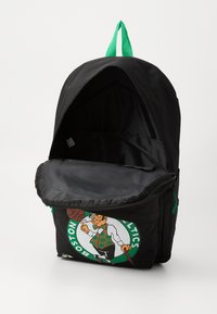Black backpack with a green zipper and handle. Features a Boston Celtics logo design on the front pocket and a spacious main compartment.