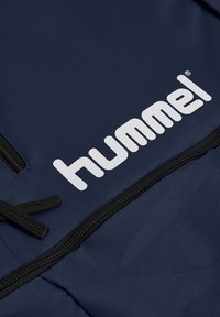 Dunkelblauer Rucksack aus strukturiertem Stoff mit einem auffälligen weißen "hummel"-Logo und schwarzen Reißverschlussakzenten.