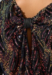 Indumento nero con paillettes, dotato di un colletto arricciato e un dettaglio a fiocco sulla parte posteriore, caratterizzato da paillettes multicolori in un motivo a spirale.