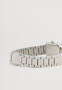 Ασημένιο ρολόι από ανοξείδωτο ατσάλι με ορθογώνια θήκη, συνδεδεμένο μπρασελέ και εγχαραγμένο κούμπωμα. Διαθέτει υφή στην επιφάνεια και κορώνα στην κορυφή.