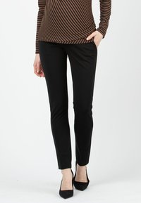 Schwarze, eng anliegende Hose mit glatter Textur und schlanker Silhouette; kombiniert mit schwarzen, spitzen Absatzschuhen, getragen mit einem braun gestreiften Oberteil.
