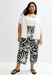 Weißes kurzes Button-Up-Hemd, schwarze und weiße gemusterte weit geschnittene Hose mit abstrahierter Gestaltung und schwarze Rutsch-Sandalen.