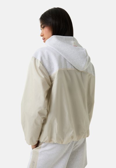 Lichte jas van een beige, waterafstotende stof met een grijze capuchon. Heeft een relaxte pasvorm en elastische manchetten voor comfort.