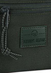 Sacchetto in tessuto verde oliva con superficie testurizzata, con etichetta in pelle verde scuro impressa con "JOHNNY URBAN" e chiusura con zip.