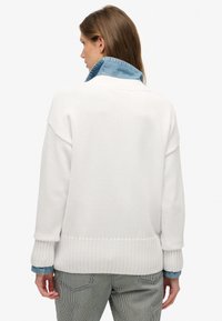 Witte gebreide trui met een geribbelde zoom en manchetten, voorzien van een blauwe denimkraag eronder. Casual en ontspannen pasvorm.