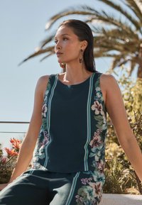 Ärmelloses türkisfarbenes Tanktop mit floralen Akzenten und vertikalen Streifen. Kombiniert mit passenden Hosen, aus glattem Stoff, lässiger Schnitt.