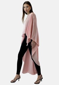 Flödande rosa cape i lätt tyg med asymmetrisk fåll, bärs över svarta leggings. Har vida ärmar och minimalistisk design.