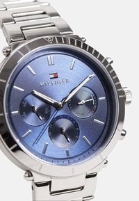 Montre en acier inoxydable avec un cadran texturé bleu, index des heures en argent, trois sous-cadrans et un bracelet maillons. Présente un logo à 12 heures.