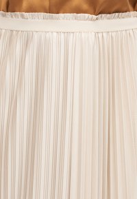 Μπεζ πλισέ φούστα με ελαστική μέση, συνδυασμένη με τοπ σε καμηλοπράσινο χρώμα που είναι μινιμαλιστικά περασμένο μέσα στη φούστα.