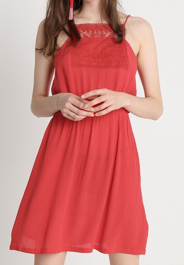 Robe rouge sans manches avec des détails en dentelle au niveau du bustier, coupe décontractée et plis légers, fabriquée en tissu léger et fluide.