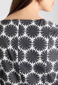 Tessuto a fiori in bianco e nero con grandi forme simili a margherite. Presenta una cerniera sul retro visibile e una superficie liscia.