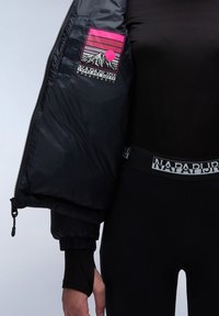 Persona che indossa leggings neri e una giacca, con un logo montano rosa e bianco all'interno della fodera della giacca e della vita, con il testo "Napapijri."