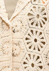 Μπεζ πλεκτό ύφασμα με λουλουδένια και γεωμετρικά σχέδια τοποθετημένα πάνω σε ριγέ καφέ ύφασμα.