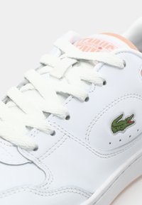 Baskets en cuir blanc avec lacets blancs, logo crocodile vert brodé et marquage rose clair sur la languette.