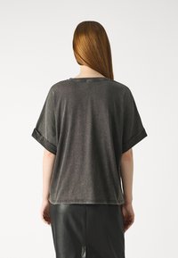 Temno siva oversize majica s krojem okroglega ovratnika, zvitimi rokavi in mehkim materialom, kombinirana s črnim usnjeni krilom.