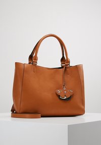 Brązowa skórzana torebka z podwójnymi uchwytami, paskiem na ramię i zawieszką w kształcie motyla przymocowaną do jednego uchwytu.