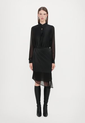 Zwarte blouse met een gestrikte hals, lange doorzichtige mouwen, gelaagde doorzichtige rok met een asymmetrische zoom, gecombineerd met hoge zwarte laarzen.