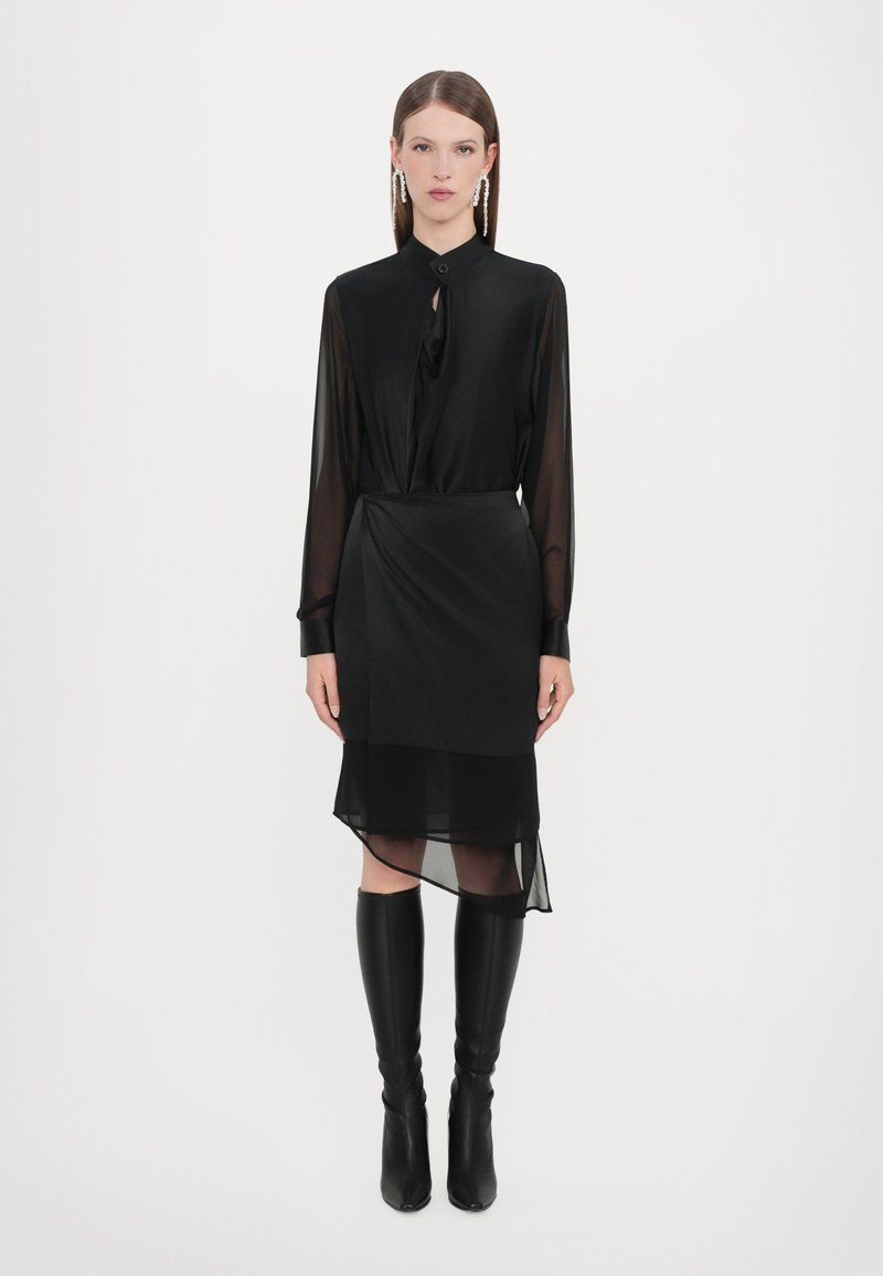 Black blouse with a tied neck, long sheer sleeves, layered sheer skirt with an asymmetrical hem, paired with high black boots.