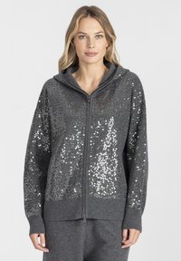 Szara bluza z kapturem zapinana na zamek, wykonana z tkaniny o fakturze, z cekinowym wzorem na przodzie. Posiada kaptur oraz ściągacze na rękawach i u dołu.