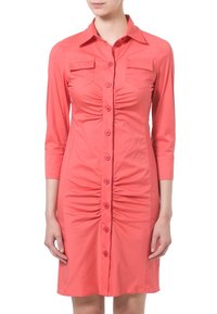 Korallinvärinen paitamekko, jossa on kaksi rintataskua, 3/4-hihat ja etuosassa poimutettua yksityiskohtaa. Sileä, kevyt kangas.