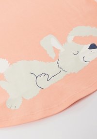 Peach-colored t-shirt with a white cartoon dog graphic lying on its back, featuring blue outlines and a light texture.