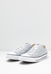 Baskets en toile grises avec lacets blancs, embout en caoutchouc, bande noire sur la semelle et doublure intérieure contrastante. Design épuré et minimaliste.