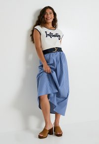 Camiseta blanca de algodón con texto "Infinity" en navy, combinada con una falda midi a rayas azules y zuecos de plataforma marrones. Un cinturón negro añade detalle.