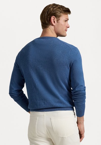 Blauwe gebreide trui met lange mouwen en een ronde halslijn. Zachte textuur met een subtiel patroon. Gedragen met lichtgekleurde broeken.