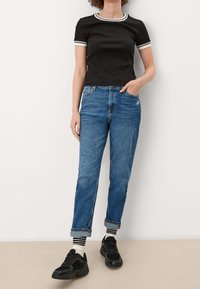 Černý žebrovaný top s krátkým rukávem a bílým lemem, doplněný o distressed modré džíny s ohrnutými rukávy a černé tenisky s bílými a  černými pruhovanými ponožkami.