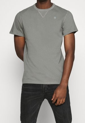 Graues T-Shirt mit kurzen Ärmeln und Rundhalsausschnitt, das über kontrastierende Nähte und ein kleines Logo auf der Brust verfügt. Aus Baumwolle, lässiger Schnitt.