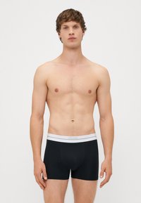 Boxeri negri cu talie elastică albă. Material neted, design ajustat, lungime scurtă a piciorului și detalii de cusătură minime.
