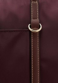 Donker bordeauxkleurige tas met een gladde stof en een gestructureerde bruine schouderband, accentueert met gouden hardware en opvallende stiksels.