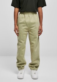 Light green sweatpants with an elastic waistband and cuffs, featuring subtle side stitching details. Paired with white sneakers.
