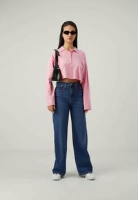 Izgriezta rozā garām piedurknēm polo krekla, augsto jostasvietu zili džinsi, balti apavi, melni saulesbrilles un mazs melns soma. Gluda auduma un brīvs piegriezums.