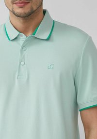 Polohemd in hellmintgrün aus strukturiertem Stoff. Mit einem Kragen mit dunkelgrünen Akzenten und einem dezenten Logo auf der Brust.