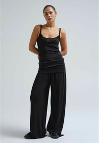 Schwarzes, ärmelloses Tanktop mit dünnen Trägern, kombiniert mit lockeren, schwarzen Hosen. Beide Kleidungsstücke haben eine weiche, glatte Textur und eine entspannte Passform.