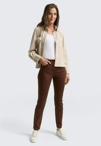 Beige corduroy blouse met knopen, witte tanktop, bruin slim-fit broek en witte sneakers, weergegeven op een neutrale achtergrond.