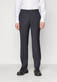 Donkergrijze, op maat gemaakte broek van gladde stof, met een recht model en een vlakke voorkant, gecombineerd met zwarte veterschoenen.