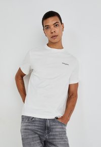 Hvit bomulls T-skjorte med rund hals og korte ermer, med en liten svart "Pepe Jeans" logo på brystet. Myk tekstur, klassisk passform.