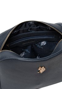 Schwarze Lederhandtasche mit navy-farbenem Innenfutter, Reißverschlusstaschen und goldfarbenem Logoakzent. Texturiertes Material und strukturierte Form.