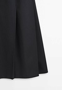 Jupe noire trapèze avec un design plissé, tissu lisse et ourlet évasé sur fond blanc.