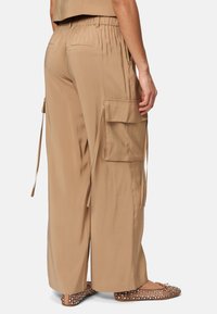Beige wijde cargobroek van lichtgewicht stof, met zijzakken, trekkoorddetails en een ontspannen pasvorm, gecombineerd met platte schoenen.
