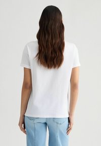 T-shirt bianco in cotone con maniche corte arrotolate, vestibilità rilassata e collo girocollo, abbinato a jeans di denim chiaro. Design minimalista, senza decorazioni.