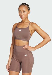Hnedý športový crop top a šortky s vysokým pásom, s hladkou textúrou a bielymi logovými akcentmi na oboch kusoch.