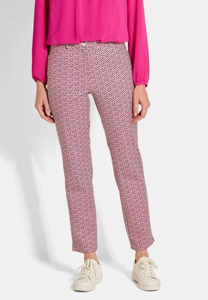 Pantaloni a fantasia in una tonalità di rosa chiaro con un design geometrico, abbinati a una maglietta rosa vivace e sneakers bianche.