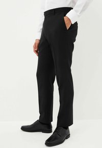 Schwarze Anzughose mit gerader Beinform, seitlicher Tasche und Bund. Kombiniert mit schwarzen Lederschuhen und einem weißen Hemd mit Knöpfen.