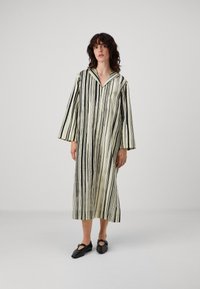 Rochie lungă în dungi, de culoare crem și negru, având guler și mâneci largi. Materialul pare neted și are o croială lejeră.